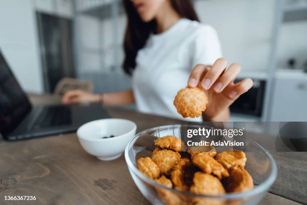 close up of young asian woman snacking on healthy rice crisps while using laptop for online learning. continuous online learning, self-enhancement. healthy snacks with healthy eating lifestyle. enhances work productivity - crackers stock pictures, royalty-free photos & images