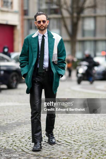 Isaac Hindin-Miller wears sunglasses, a white and pale blue striped print pattern shirt, a dark green embossed pattern tie, a dark green oversized...