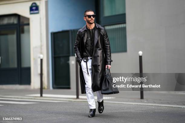 Pelayo Diaz wears black sunglasses, silver earrings, a gold chain necklace, a black / gray / beige print pattern t-shirt, a matching black / gray /...