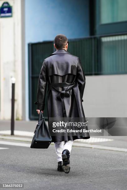 Pelayo Diaz wears black sunglasses, silver earrings, a black shiny leather long coat, a black shiny leather large Birkin handbag from Hermes, white...