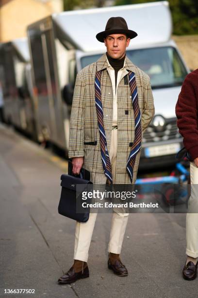 Filippo Cirulli wears a brown felt hat, a brown ribbed turtleneck pullover, a white shirt, a yellow / beige / blue small checkered print pattern long...