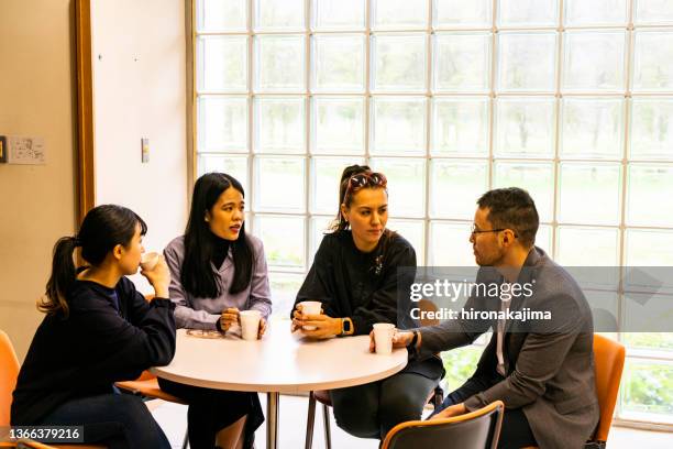 a group of four asians meet over a cup of coffee at a round table. - round table stockfoto's en -beelden