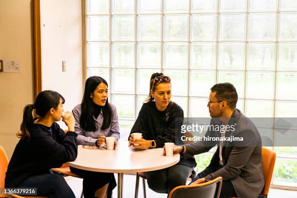 a group of four asians meet over a cup of coffee at a round table. - round table imagens e fotografias de stock
