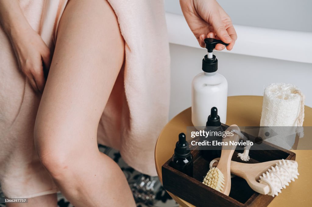 Body skin care after the shower, a young woman applies a moisturizing lotion on her body. Female Beauty routine. Home care products for the skin of the face, body and hair. Moisturizing and cleansing the skin, massage brushes.