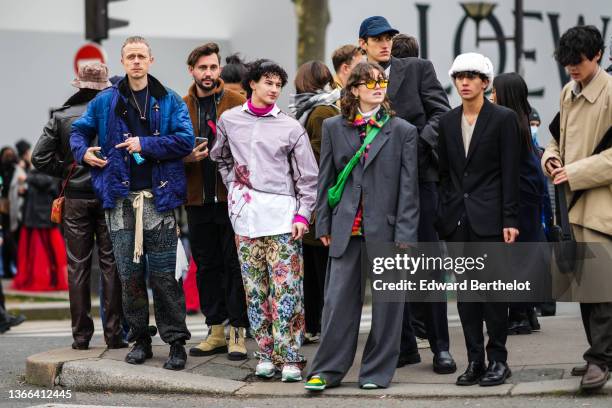 Guest wears black and orange sunglasses, a white turtleneck pullover, a black / neon green / pink / yellow print pattern shirt, a neon green shiny...