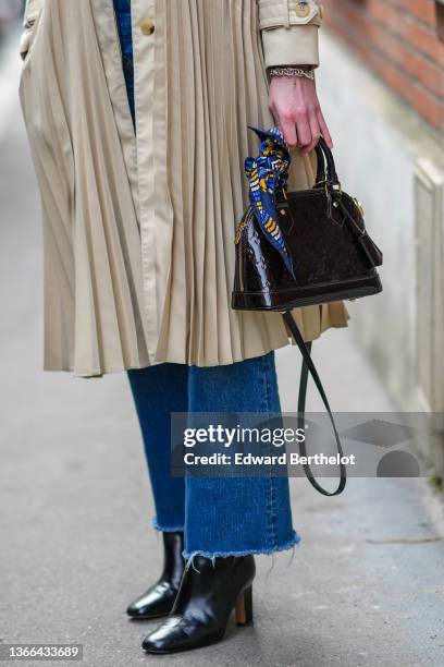 Guest wears a beige pleated trench coat from Sandro, navy blue denim ripped flared jeans pants, a navy blue with blue / yellow / white print pattern...