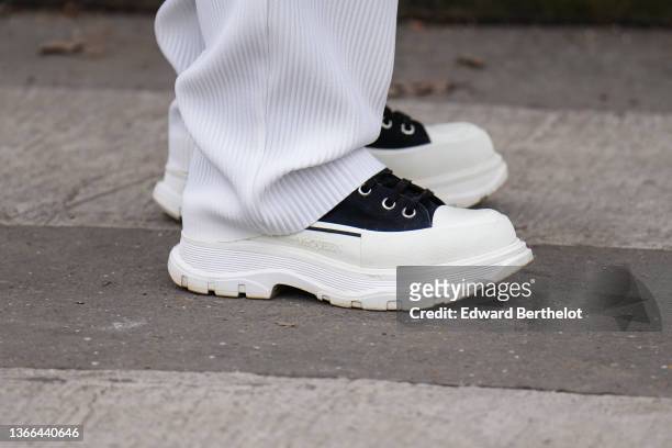 Guest wears white ripped flowing pants, black fabric and white plastic platform soles sneakers from Alexander Mc Queen, outside Loewe, during Paris...