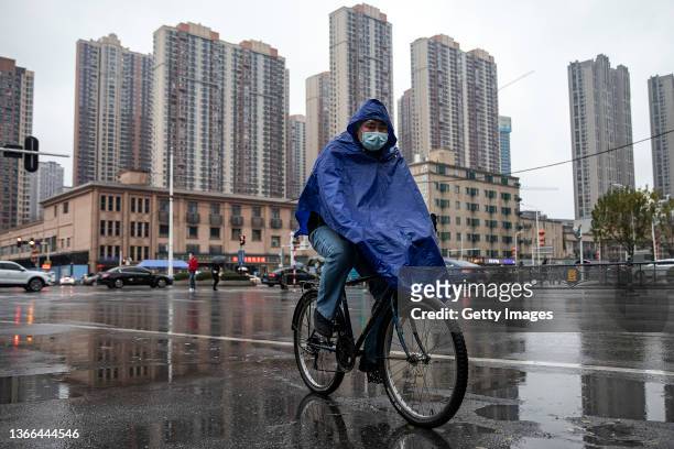 People wearing face masks travel along a street in front of a closed of Huanan seafood market during the rain on January 23, 2022 in Wuhan, China....