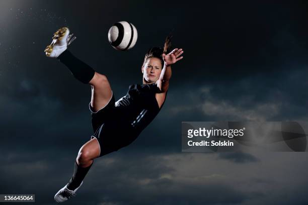female football player kicking ball in mid air - woman football stock-fotos und bilder
