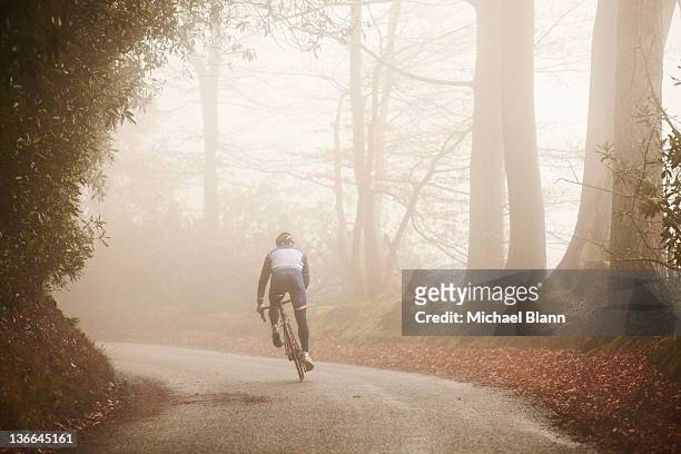 competitive cyclist riding along foggy road - forward athlete stock pictures, royalty-free photos & images