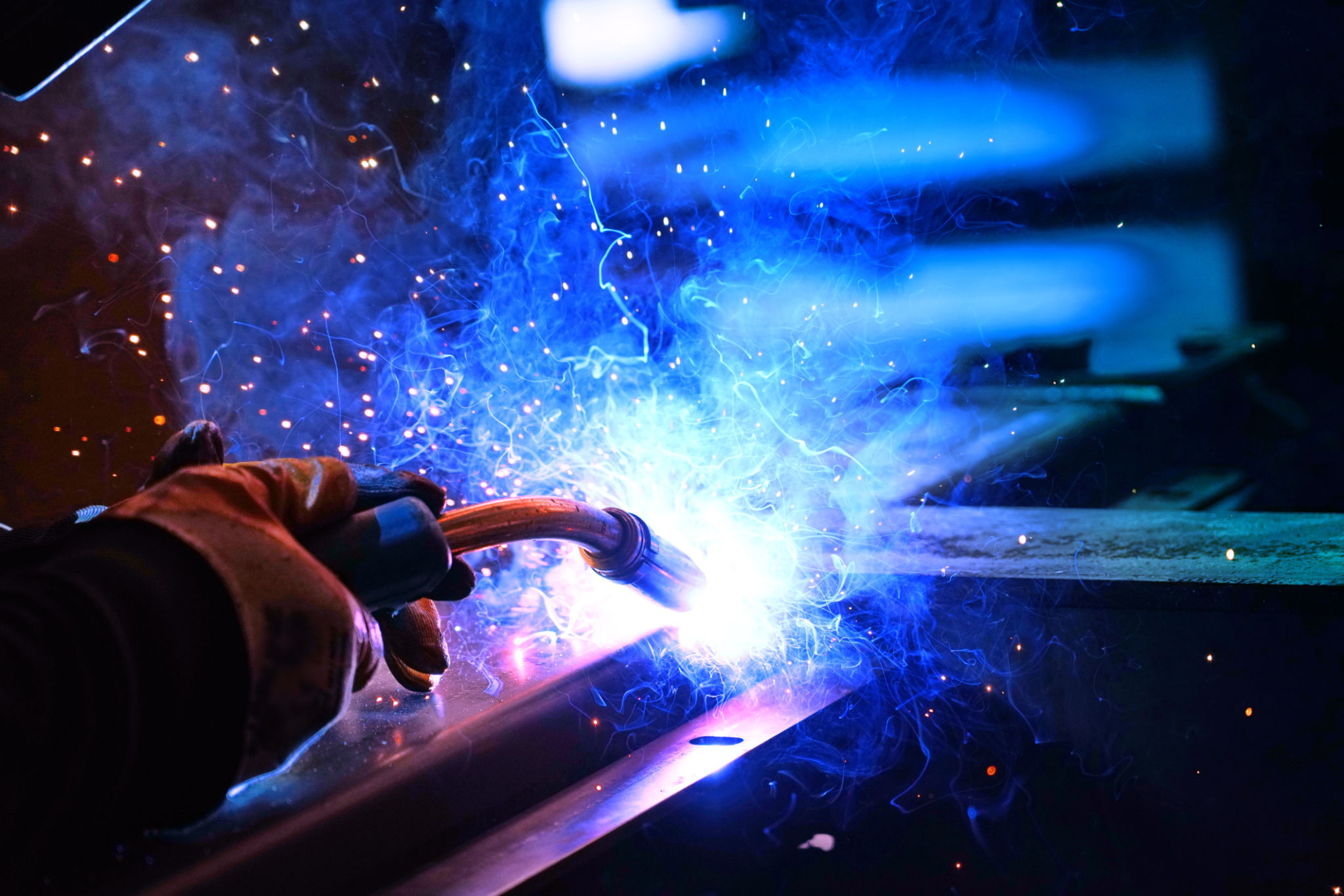 A welder welds metal into his workshop. Blue welding sparks. Gas combustion and blue smoke. Small welding workshop. Welding juncture of metal construction A welder welds metal into his workshop. Blue welding sparks. Gas combustion and blue smoke. Small welding workshop. Welding juncture of metal construction