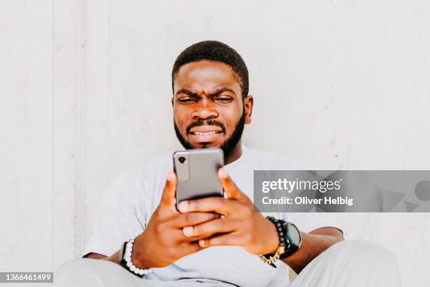young man makes a disgusted grimace while looking at his smartphone - afkeer stockfoto's en -beelden