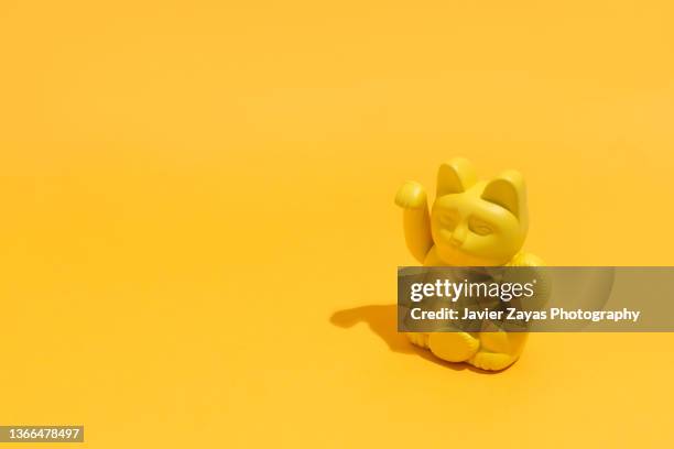 lucky cat (maneki neko) against yellow background - maneki neko stock pictures, royalty-free photos & images