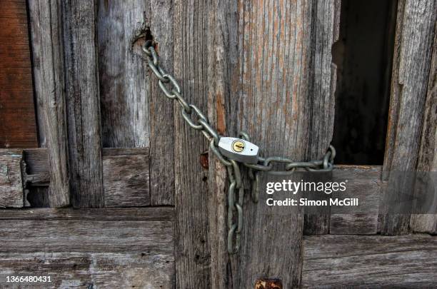 chained and padlocked old rotting wooden double doors of an abandoned building - okupas fotografías e imágenes de stock