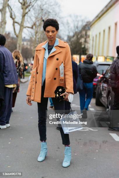 Model Janaye Furman wears a caramel belted peacoat over a baby blue leather jacket, skinny black jeans, baby blue lace-up booties, and holds a small...