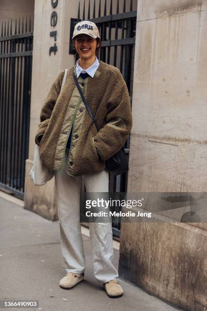 Model Adele Aldighieri wears a light colored Paris cap, green sherpa jacket, white pants, and Birkenstock clogs outside the Kenzo FW22 show on...