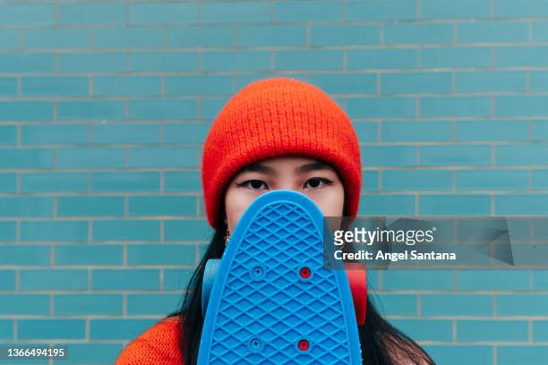 cool asian woman hiding her face with a skateboard - disinvolto foto e immagini stock