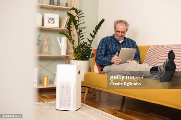 man turning on air humidifier using a digital tablet - air purifier stock pictures, royalty-free photos & images