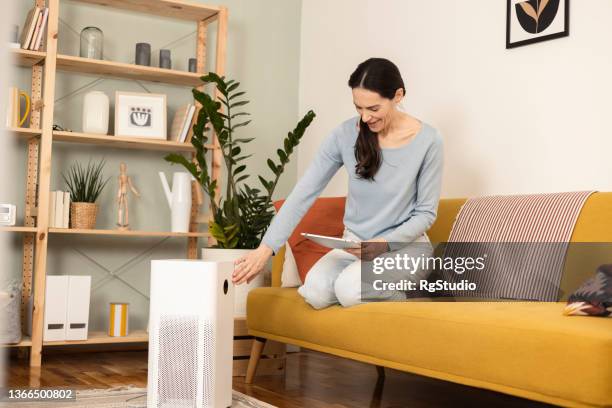 mulher madura ligando umidificador de ar usando um tablet digital como controle remoto - humidifier - fotografias e filmes do acervo