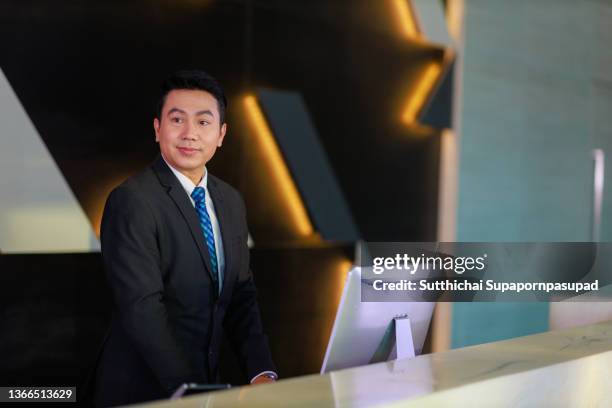 a male hotel manager standing in front of the lobby reception counter. - asian receptionist stock pictures, royalty-free photos & images