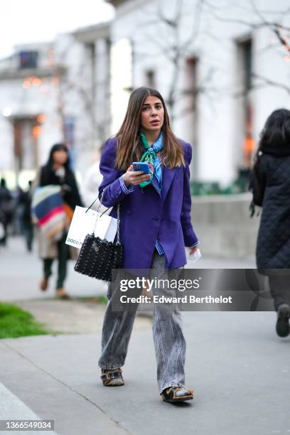 Héloïse Salessy wears a green and blue with black and white print pattern silk scarf, a blue purple oversized blazer jacket, gold rings, a black...