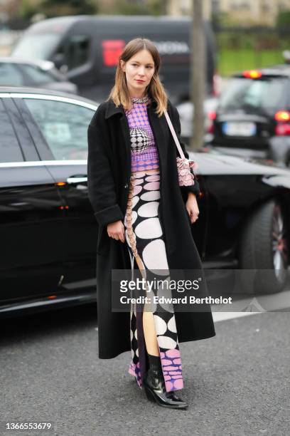 Diane Rouxel wears a large silver chain necklace, a purple and pink circle print pattern with black and white details, a black long coat, a pink...