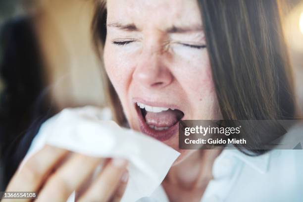 woman sneezing loud with open mouth behind a window. - sneezing stockfoto's en -beelden