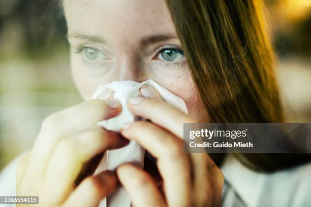 woman sneezing behind a window. - handkerchief fotografías e imágenes de stock