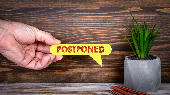 POSTPONED. Yellow speech bubble in a man"s hand on a wooden background