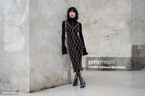Xiayan wears a black ribbed turtleneck buttoned / long flared sleeves midi dress, large gold chain earrings, a gold chain checkered long dress, a...