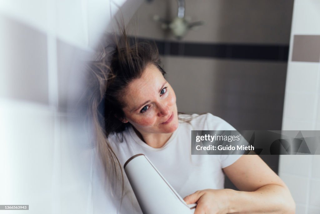 Woman drying her hair at home in bathroom.