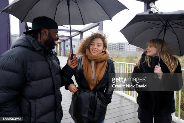 friends enjoying time together in an outside work environment - white and black women and umbrella stockfoto's en -beelden