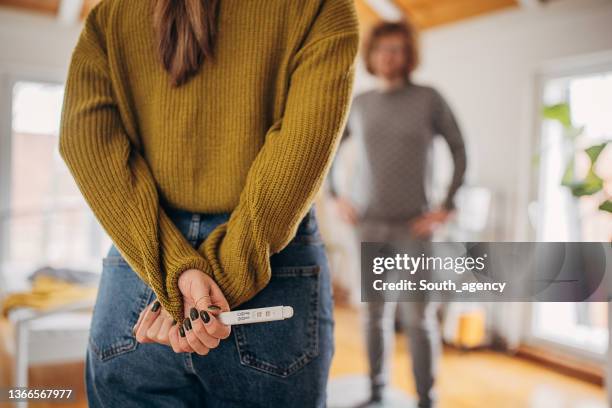 une jeune femme surprend son petit ami avec un test de grossesse positif - hands behind back stock photos et images de collection