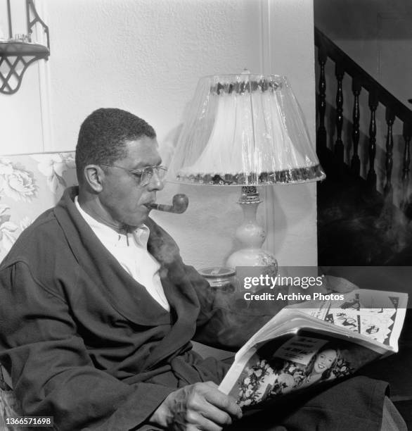 Man smoking a pipe as he reads a newspaper in his dressing gown at home, US, circa 1950.