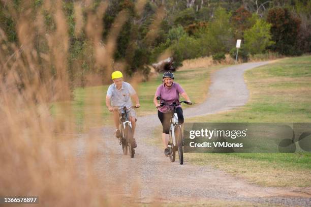 people riding electric bikes and running through park - adult riding bike through park stock pictures, royalty-free photos & images