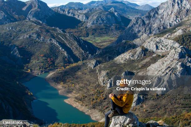 rear view of sitting woman with wool hat contemplating the landscape of reservoir in the mountain - provincia de león fotografías e imágenes de stock