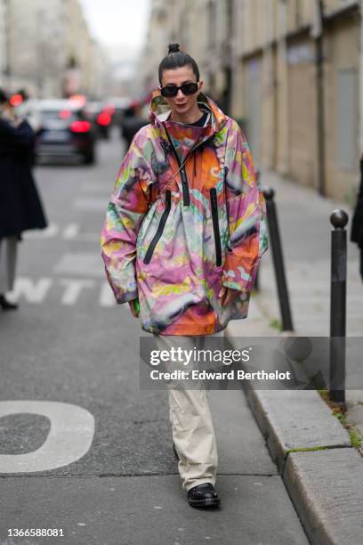 Guest wears black sunglasses from Versace, a purple / pale green / orange / neon yellow print pattern hoodie / high neck oversized rain coat, white...