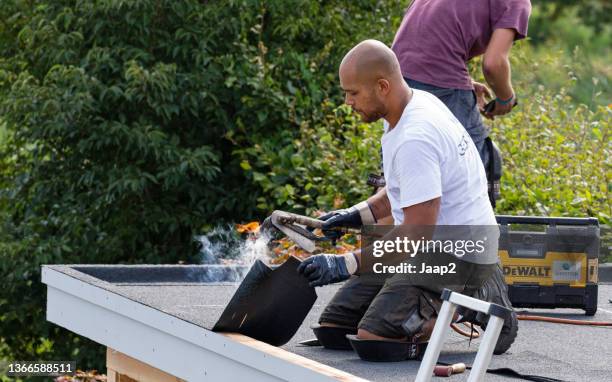 two roofers applying bituminous roofing asphalt on a domestic garden shed - holland achtertuin stockfoto's en -beelden