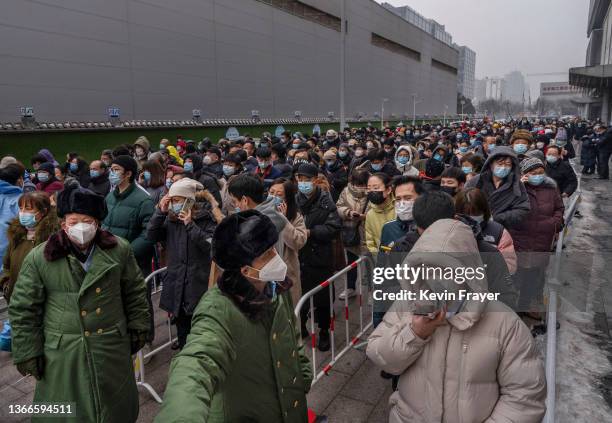 Security stand in front of people as they line up for nucleic acid tests to detect COVID-19 at a mass testing site on January 24, 2022 in Beijing,...