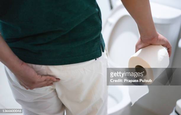man holding toilet paper roll in bathroom - hemorrhoid stock-fotos und bilder