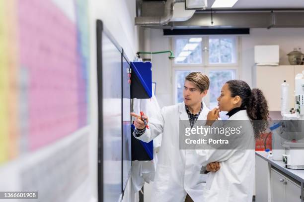 zwei forscher diskutieren über chemische formel auf whiteboard - scientist standing stock-fotos und bilder