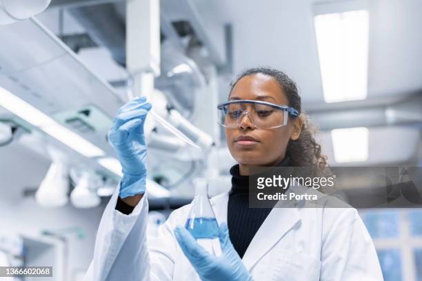 woman scientist experimenting with chemicals in lab - black glove stock pictures, royalty-free photos & images