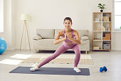 Happy young woman in activewear doing lateral lunges during fitness workout at home