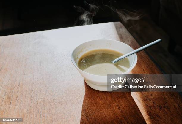 simple image of a bowl of steaming hot soup on a wooden surface - scodella per zuppa foto e immagini stock