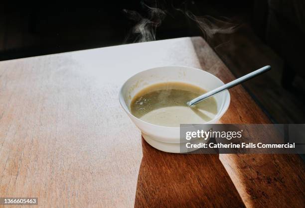 simple image of a bowl of steaming hot soup on a wooden surface - soup bowl stock pictures, royalty-free photos & images