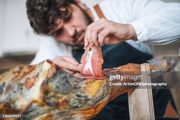 professional cutter carving slices from a whole bone serrano jamon. - delicatessen stock pictures, royalty-free photos & images