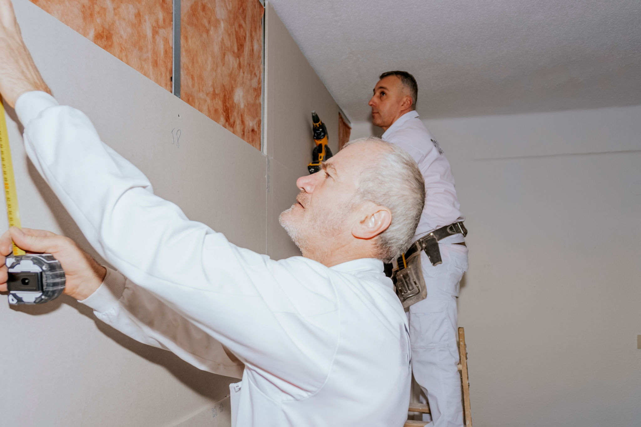 Two workers installing plasterboard panels with acoustic insulation. Two workers installing plasterboard panels with acoustic insulation.