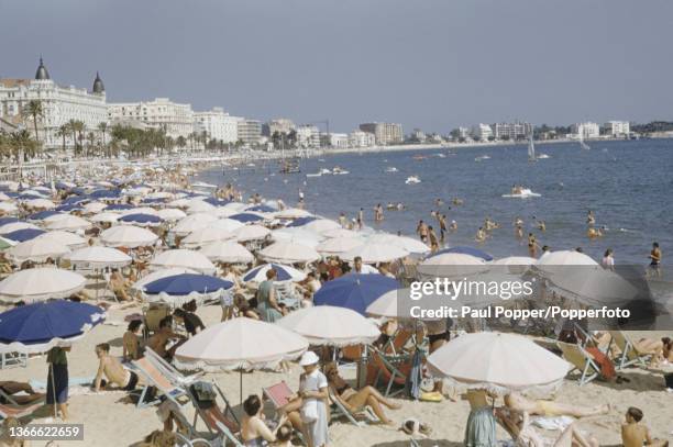 Visitors swim in the sea and lie on sun loungers under umbrellas on the beach in front of villas and hotels, including the Carlton Hotel on top left,...