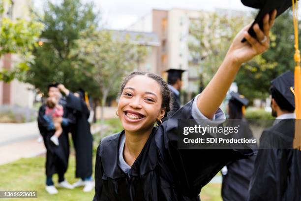 excited young adult graduate raises cap in hand - graduates stockfoto's en -beelden