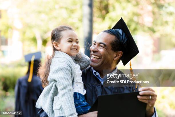 little girl makes graduating grandfather laugh with silly face - adult student stock pictures, royalty-free photos & images